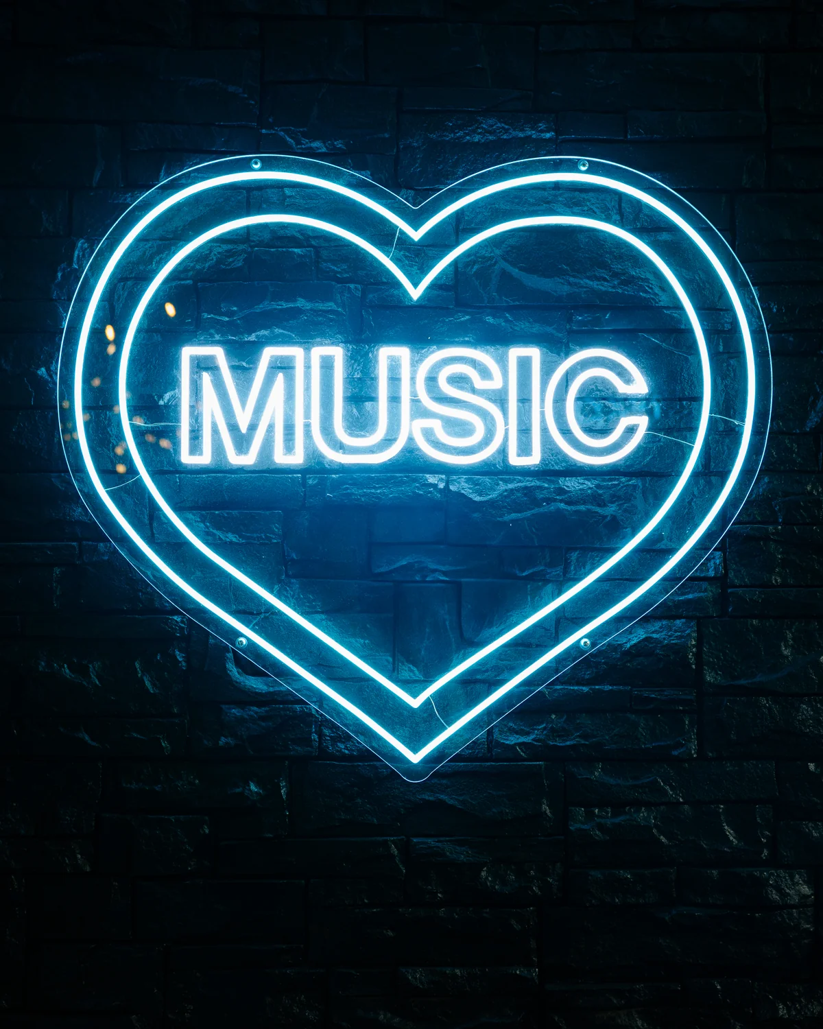 A glowing teal neon heart with the word MUSIC inside it, mounted on a textured dark brick wall