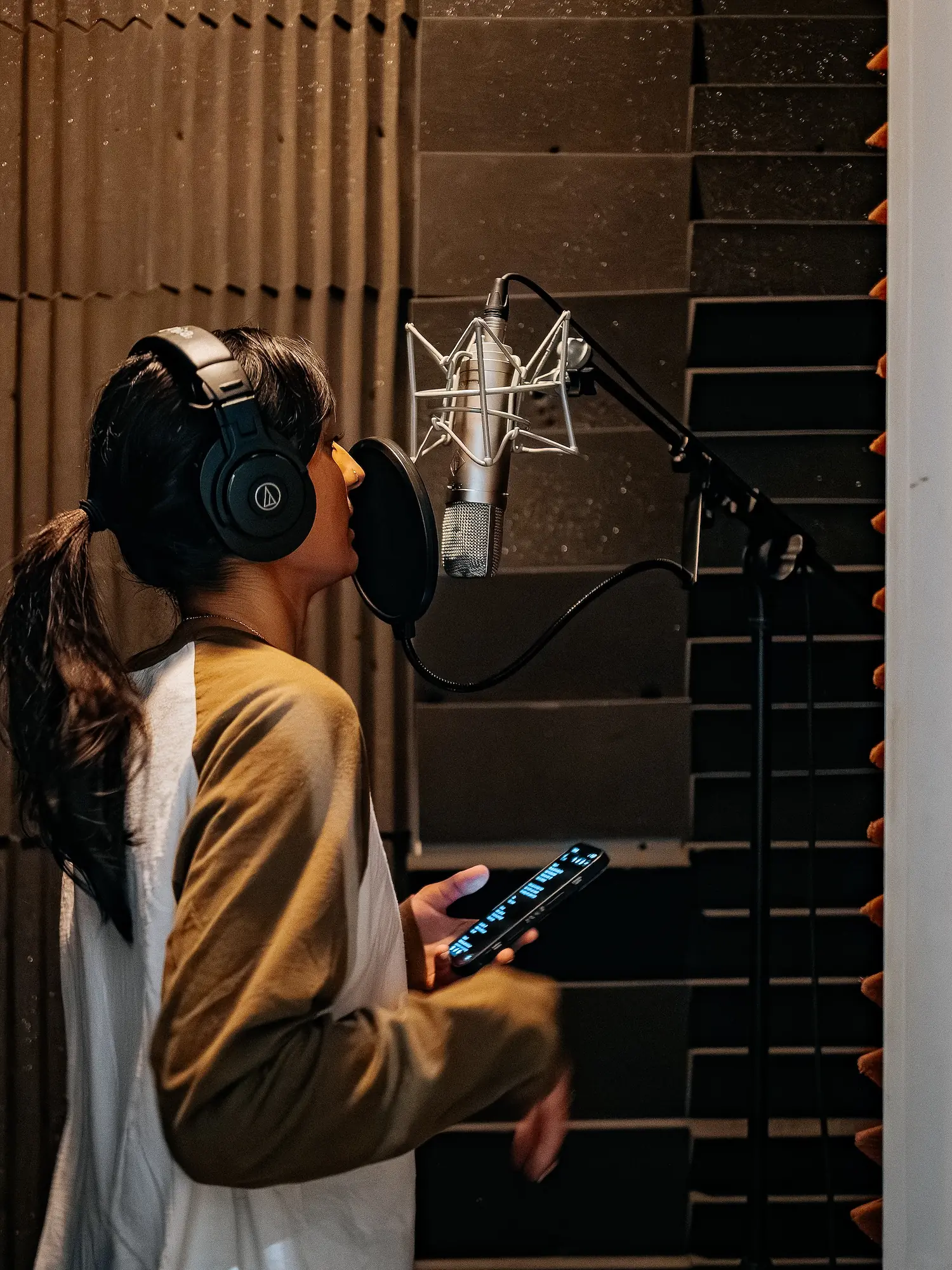 Vocalist recording in the Resonate vocal booth with headphones and large-diaphragm microphone